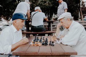 Two men sit outdoors playing chess for their aged care activities