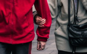 One person holds the arm of another elderly person as they help each other in the street